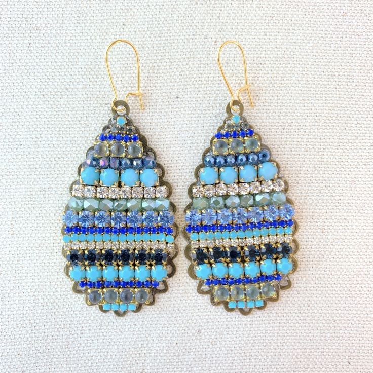 "Dive into these dramatic teardrop statement earrings in exotic sea-inspired blue tones. Perfect rows of stunning Swarovski rhinestones and glass beads mounted on tear-drop metal filigree stampings in an antique bronze finish create a perfect blue-tone statement earring to add a pop of color. Lightweight. 3\"L x 1.25\"W. Gold-plated, nickel-free ear wires. Handmade in USA." Blue Jeweled Metal Earrings, Bohemian Jeweled Beaded Drop Earrings, Blue Beaded Drop Earrings, Blue Embellished Jewelry For Party, Blue Teardrop Jeweled Jewelry, Bohemian Blue Beaded Teardrop Earrings, Blue Teardrop Earrings With Dangling Beads, Blue Jeweled Teardrop Earrings, Bohemian Beaded Blue Teardrop Earrings