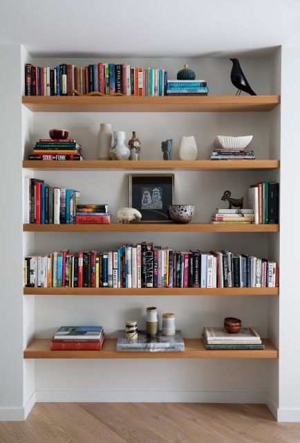 a bookshelf filled with lots of books on top of wooden shelves next to a white wall