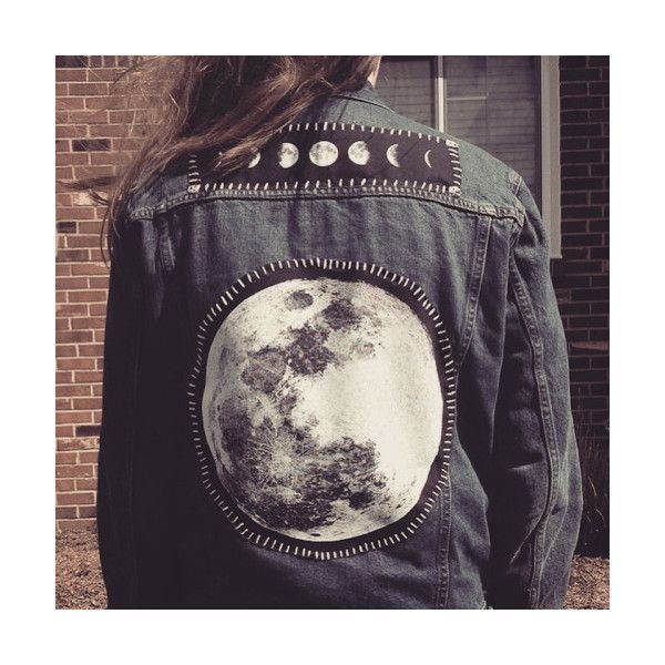 a woman wearing a denim jacket with the moon painted on it's back, standing in front of a brick building