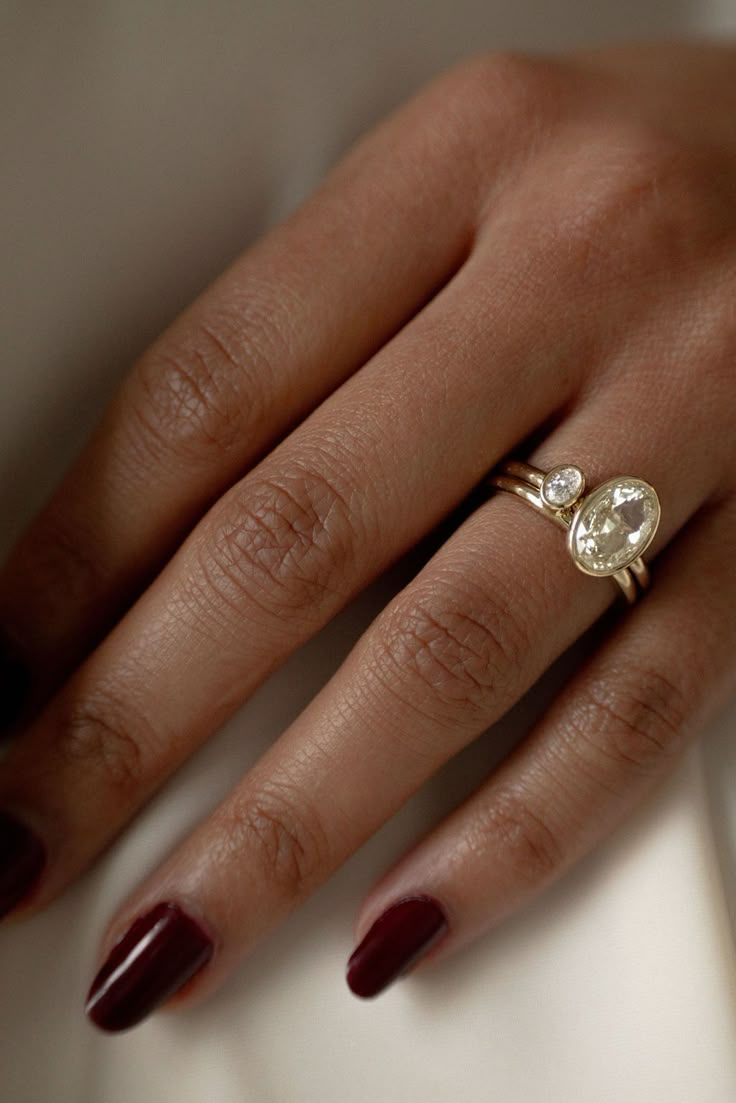 a woman's hand wearing a gold ring with an oval shaped diamond on it