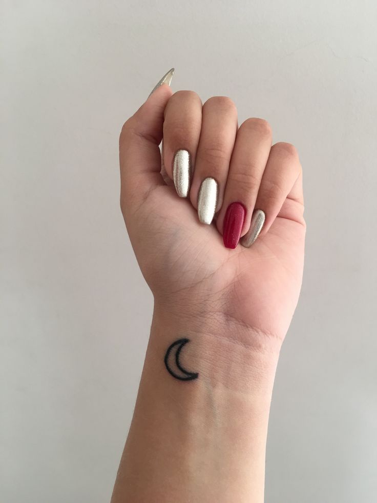 a woman's hand with two different colored nails and a crescent tattoo on the wrist