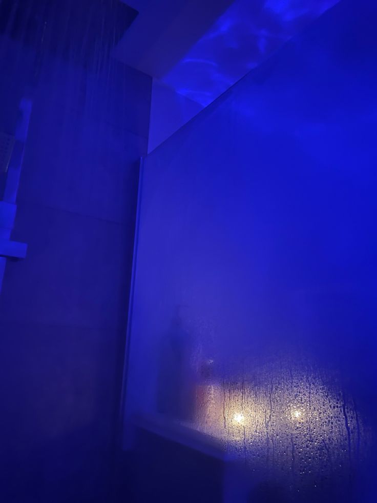 a bathroom with blue light coming from the ceiling and shower head in the corner next to the bathtub