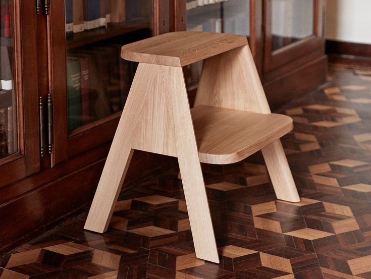 a wooden step stool sitting on top of a tiled floor next to a book shelf