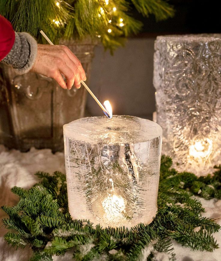 a person lighting a candle on top of a snow covered table with evergreen branches and lights