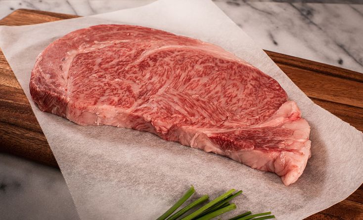 a piece of raw meat sitting on top of a wooden cutting board next to green onions