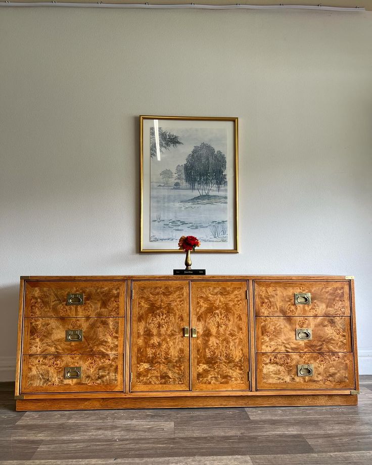 a painting hangs on the wall next to an old wooden cabinet with drawers and pulls