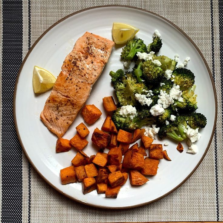 salmon, broccoli and sweet potatoes on a plate with a side of lemon wedges