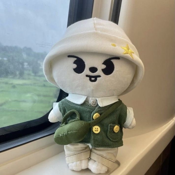 a stuffed animal is sitting on a window sill near a window with a green sweater and white hat