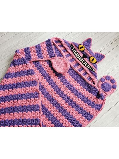 a crocheted pink and purple cat sweater laying on top of a wooden floor