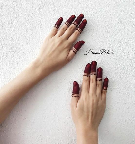 woman's hands with maroon manies and rings on their fingers against a white wall