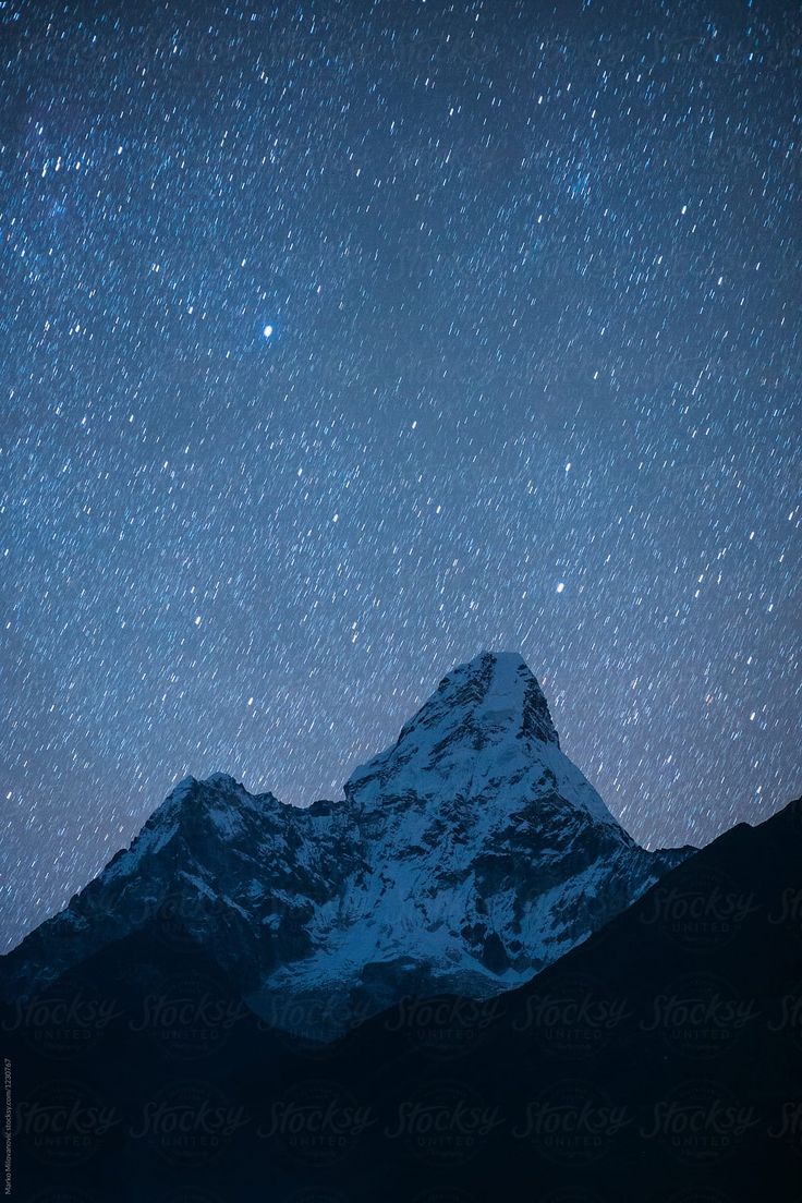 the night sky is filled with stars above a snow covered mountain and some mountains in the distance