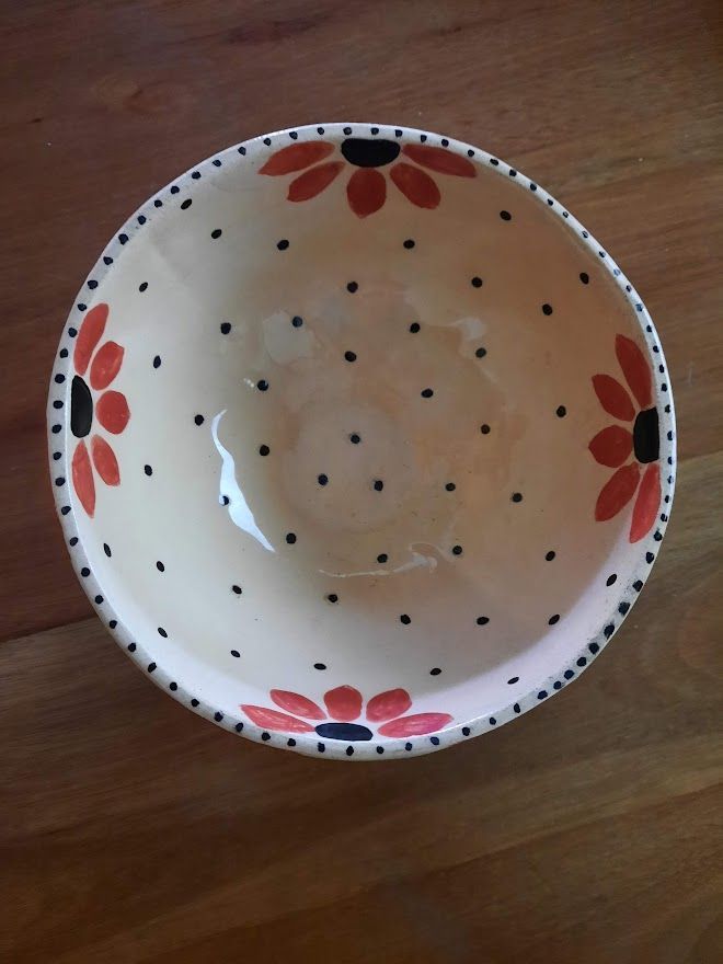 a white bowl with red and black flowers on it sitting on top of a wooden table