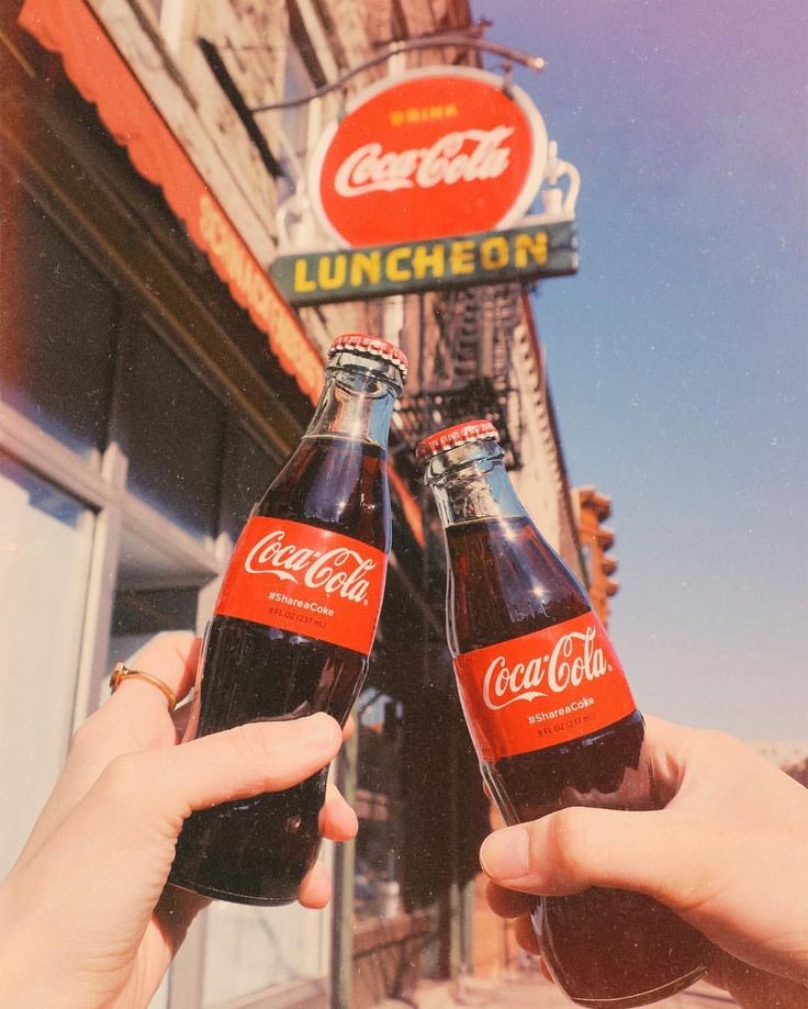 two people holding up beer bottles in front of a building