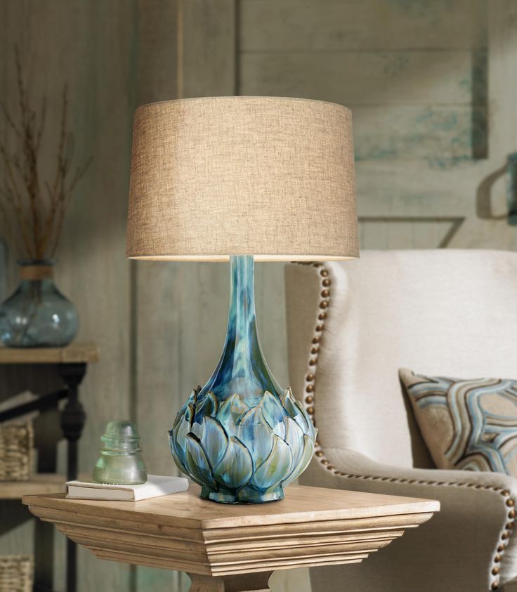 a blue vase sitting on top of a wooden table next to a white chair and lamp