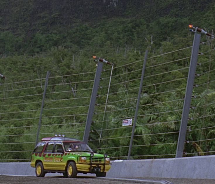 a green and yellow car driving down a road next to a tall fenced in area