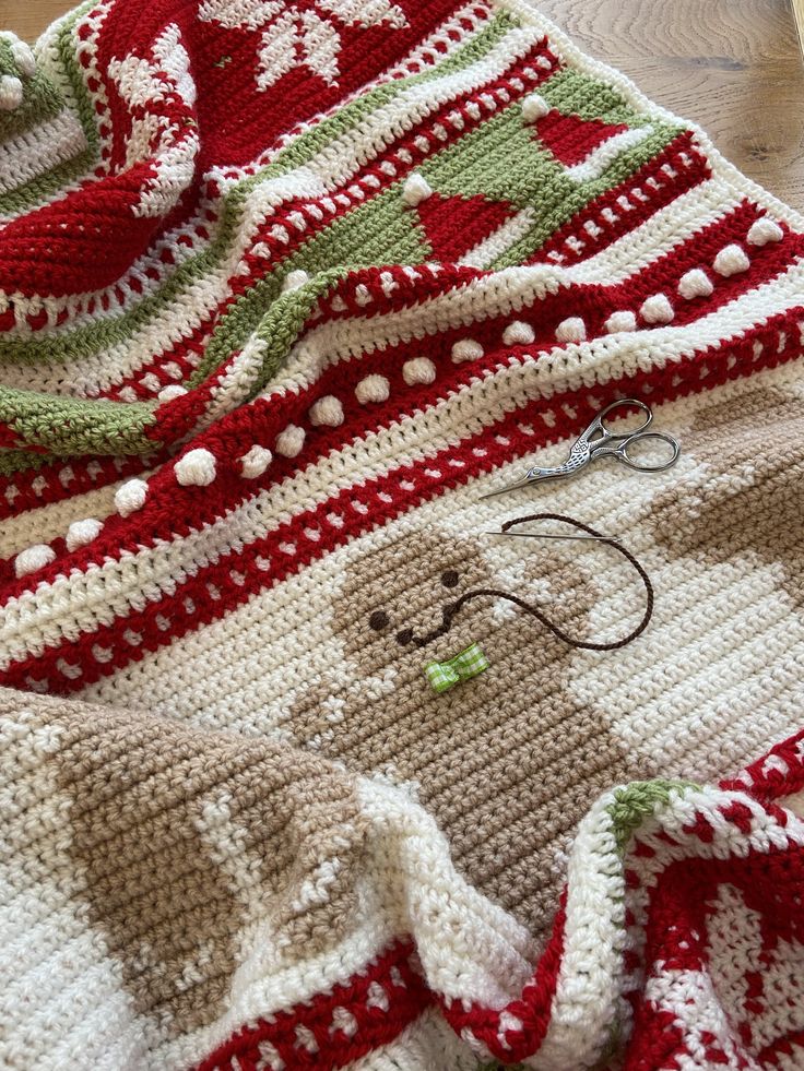 a crocheted blanket is laying on the floor next to some scissors and yarn