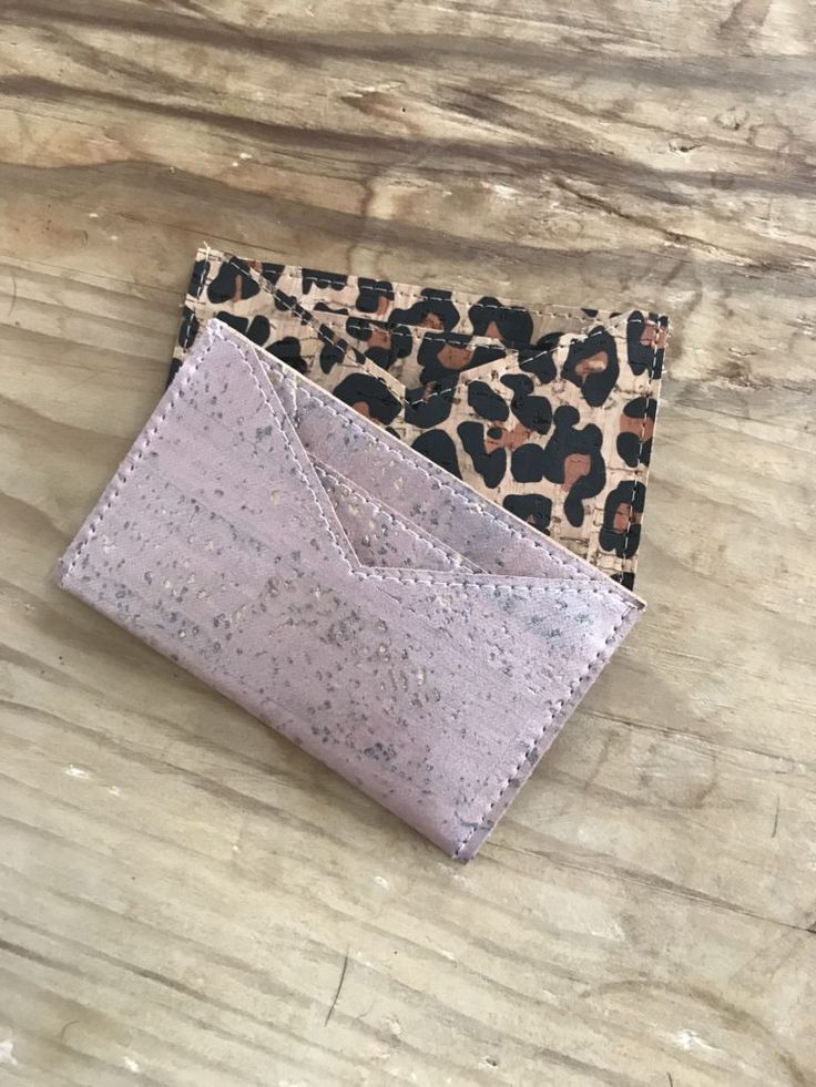 two small wallets sitting on top of a wooden table with leopard print and pink leather