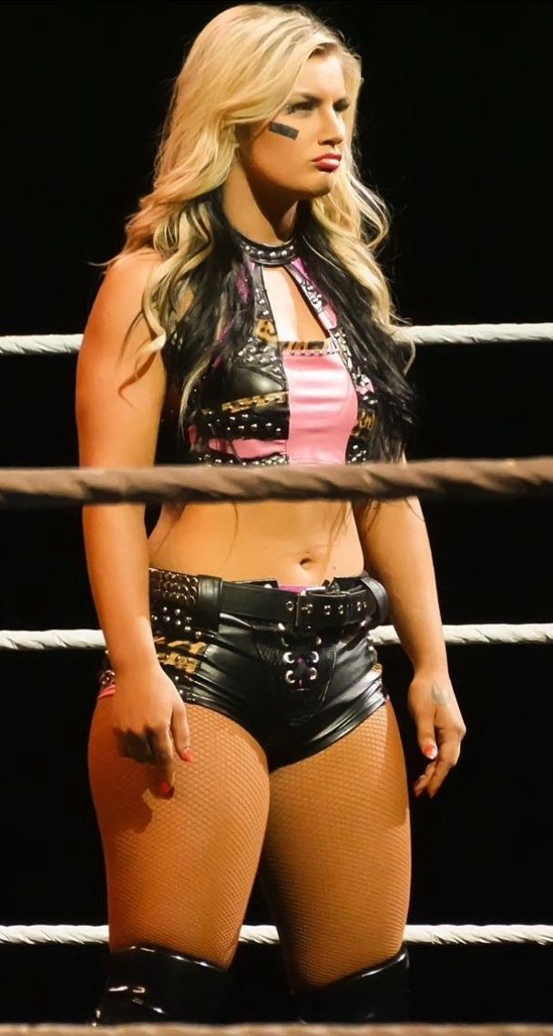 a woman in short shorts and boots standing next to a wrestling ring with her hand on her hip