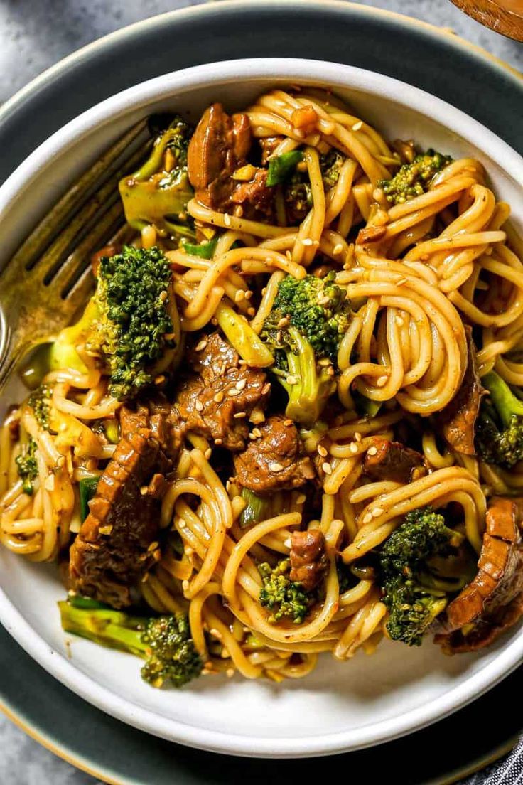 a white plate topped with pasta and meat covered in broccoli next to a fork