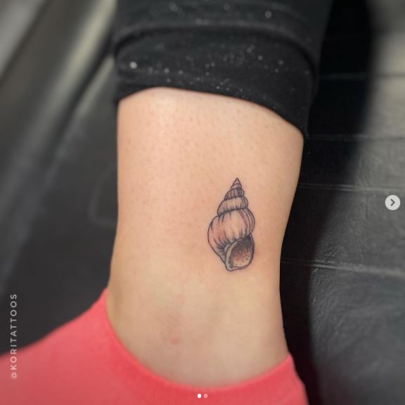 a woman's foot with a small tattoo of a shell on her left ankle