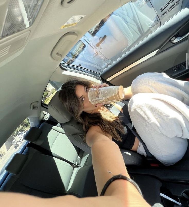 a woman sitting in the back seat of a car drinking water