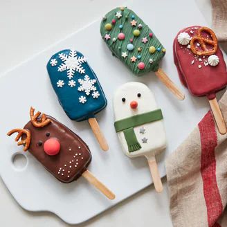 four decorated ice cream pops sitting on top of a white tray next to a plate with pretzels