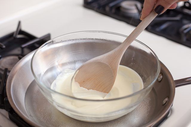 a wooden spoon in a glass bowl on top of a stove burner with yogurt