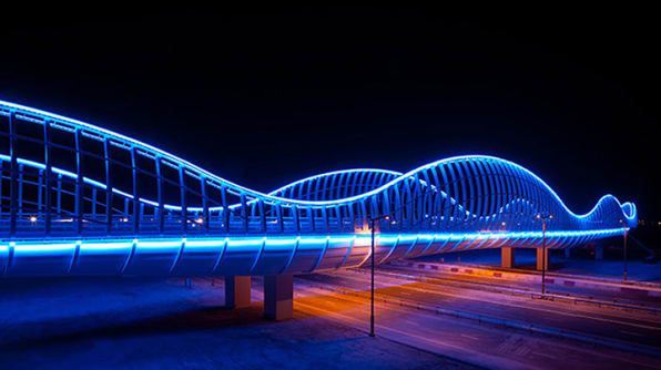 an illuminated bridge at night with blue lights on it's sides and cars passing by