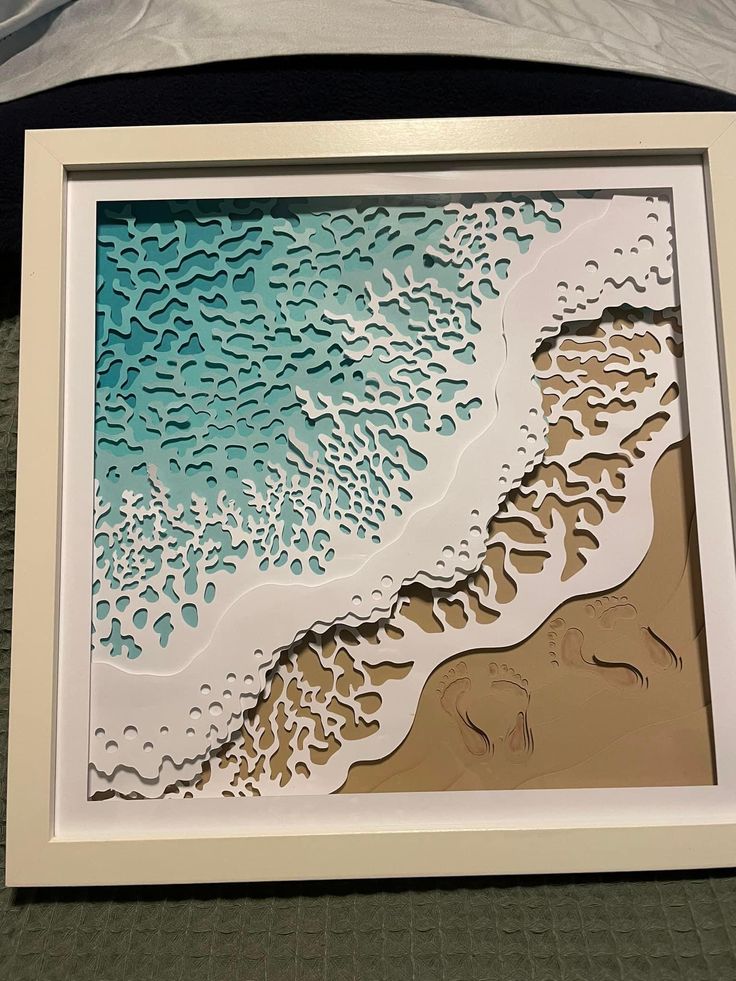 an intricate paper cut artwork depicting the beach and ocean waves in blue, brown and white