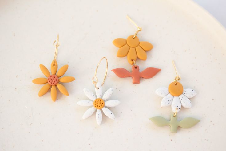 three flower shaped earrings are sitting on a white plate, one is yellow and the other is orange