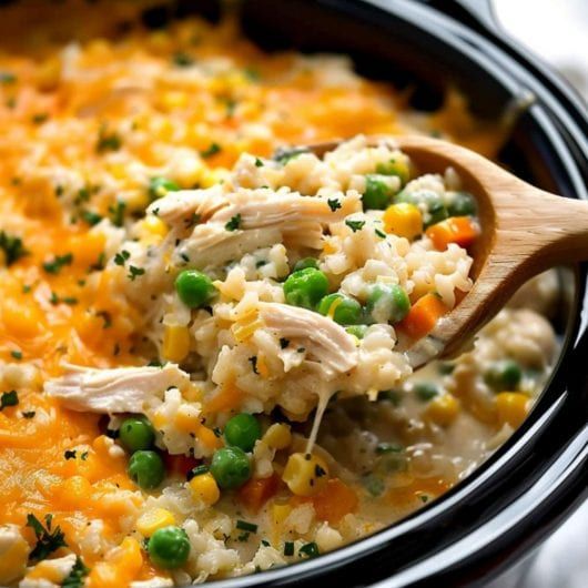 a wooden spoon scooping out some chicken and rice casserole from the crock pot