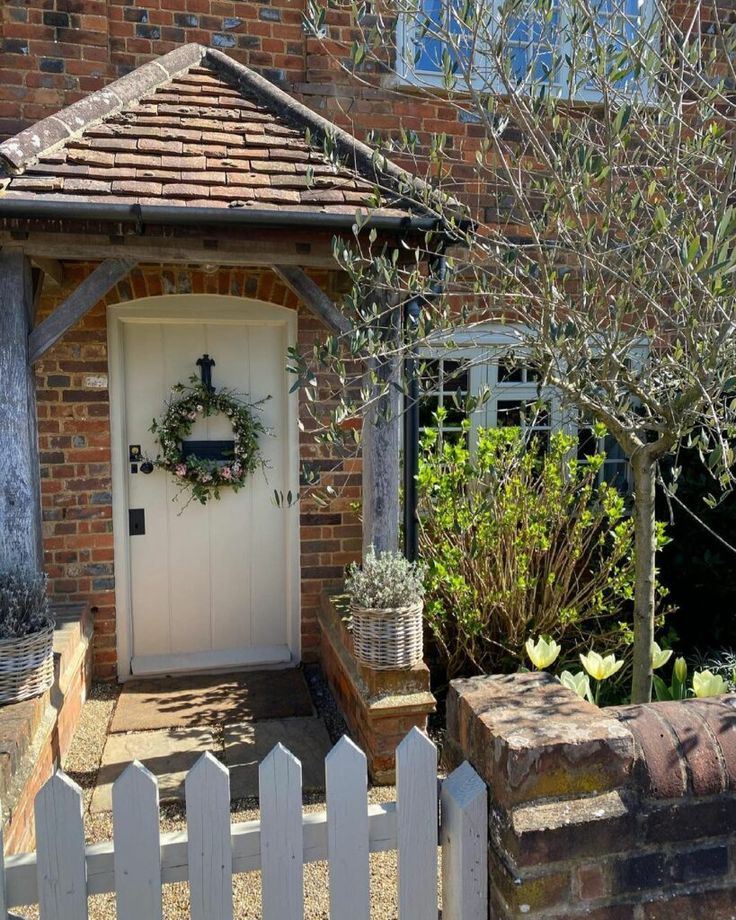 a white front door sitting next to a brick building with a wreath on it's side