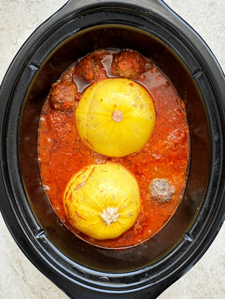 an overhead view of two cooked meatballs in a slow cooker with tomato sauce