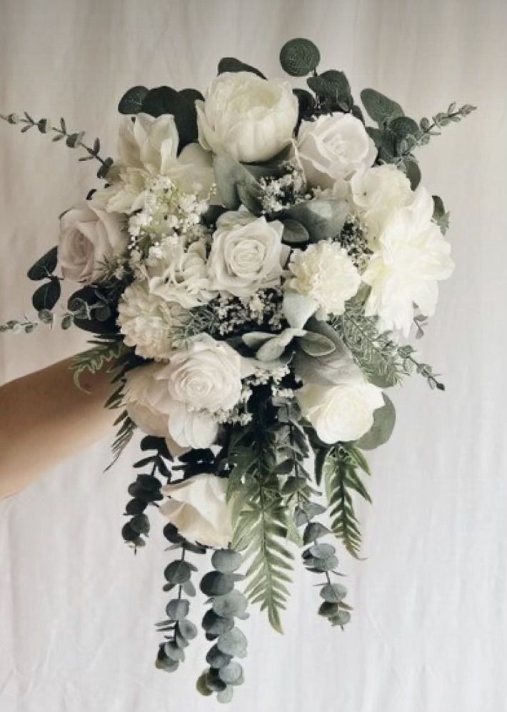 a person holding a bouquet of white flowers and greenery in front of a tweep