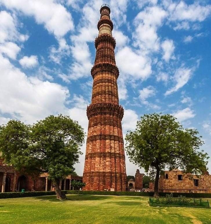 a tall brick tower sitting in the middle of a lush green field under a blue sky