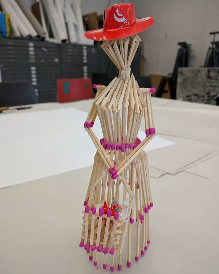 a sculpture made out of sticks and beads with a red hat on top of it