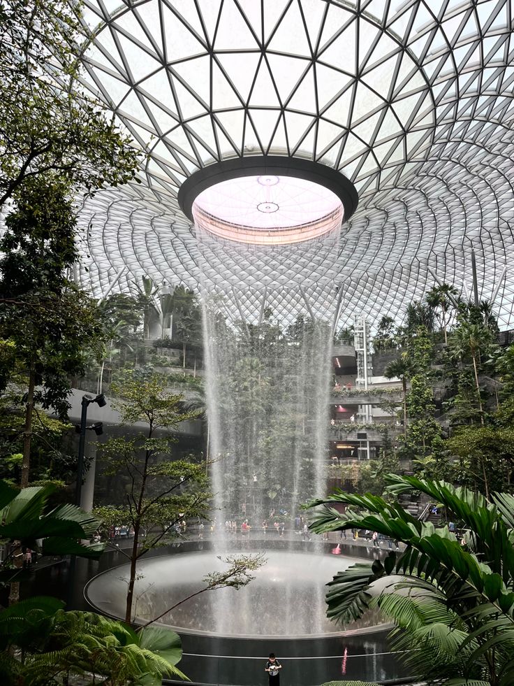 the inside of a building with a fountain in the center and lots of greenery around it