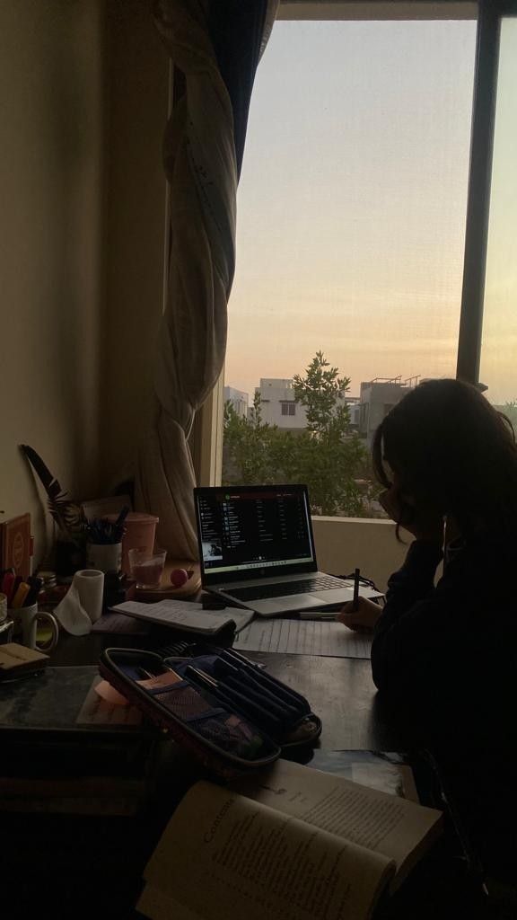 a woman sitting at a desk in front of a window with a laptop computer on it