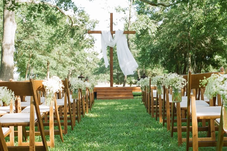 an outdoor ceremony setup with white flowers and greenery on the grass, in front of a wooden cross