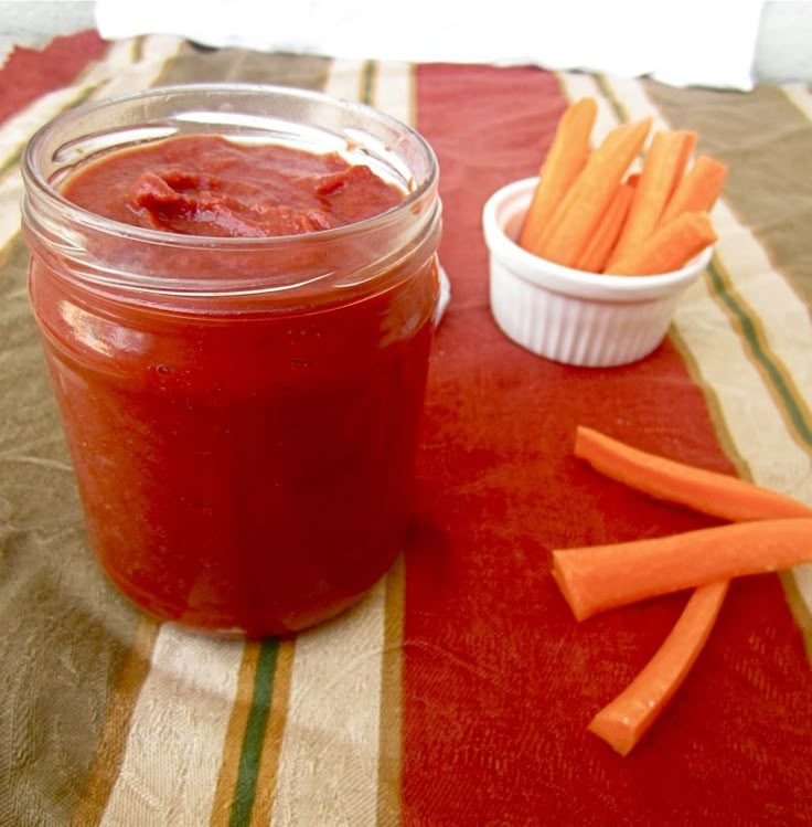 a jar filled with red sauce sitting on top of a table next to some carrots