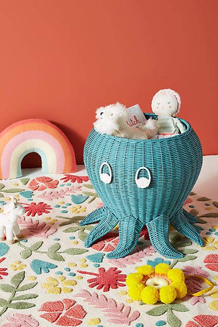 an octopus shaped basket with stuffed animals in it on a floral tablecloth next to a rainbow colored wall