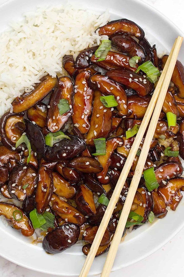 a white plate topped with meat and rice next to chopsticks on a table