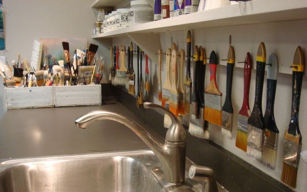 a kitchen sink with lots of paint brushes hanging on the wall above it and a metal faucet