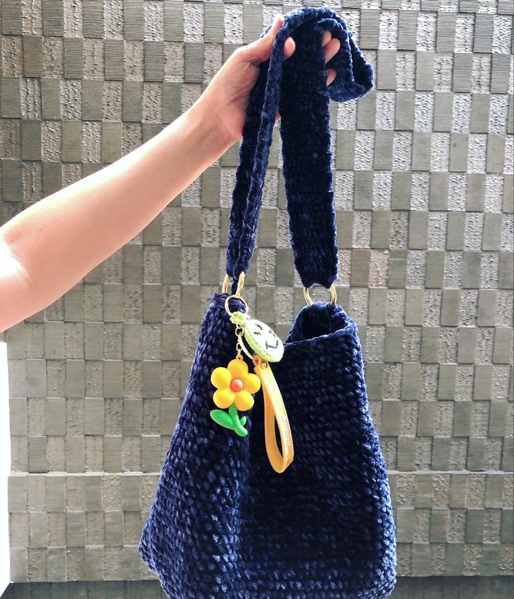 a hand holding a blue purse with a yellow flower on the handle and a small keychain attached to it