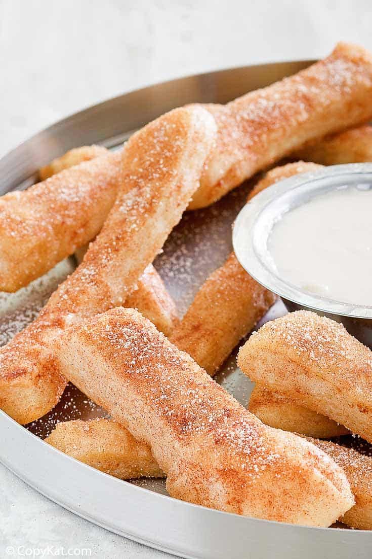 some fried food is in a metal bowl with dipping sauce on the side and powdered sugar on top