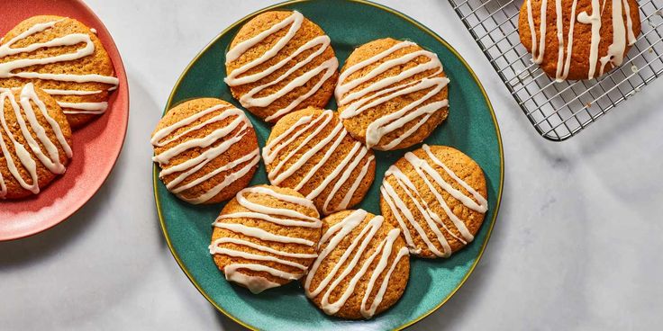 cookies with white icing are on plates next to a cooling rack