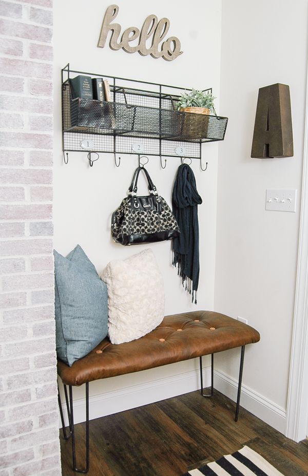 a bench and coat rack in a small room with white walls, wood flooring and black iron shelving