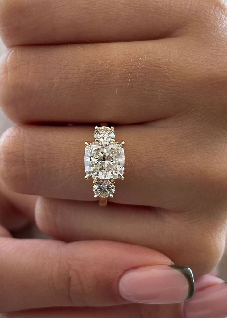 a woman's hand holding an engagement ring with three stones on the band and one stone in the middle