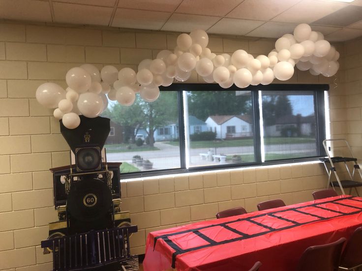 balloons are hanging from the ceiling in front of a table with red cloths on it