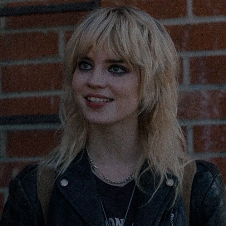 a woman standing in front of a brick wall wearing a black jacket and smiling at the camera